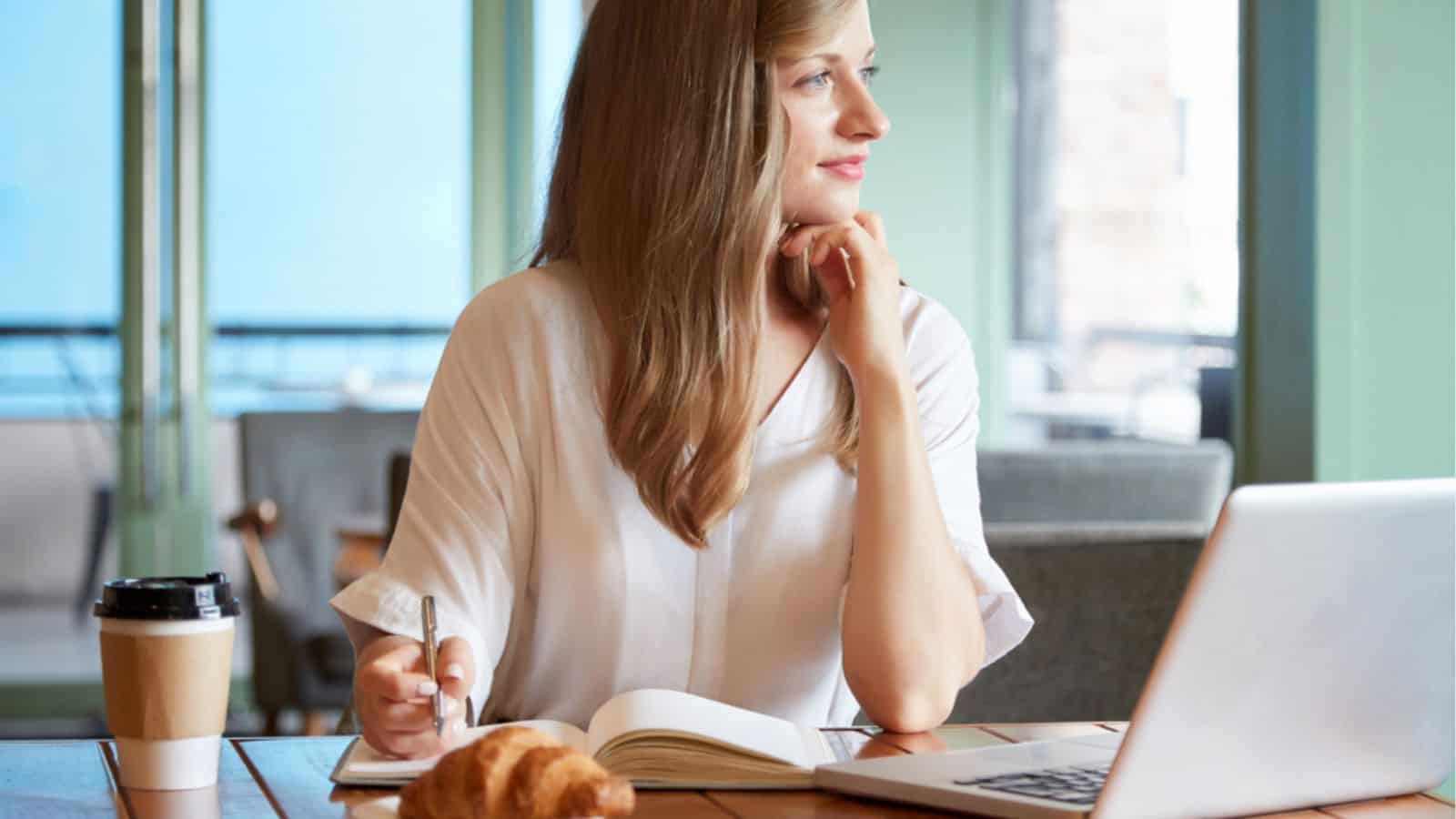 Beautiful woman thinking laptop on cafe table with coffee and croissant