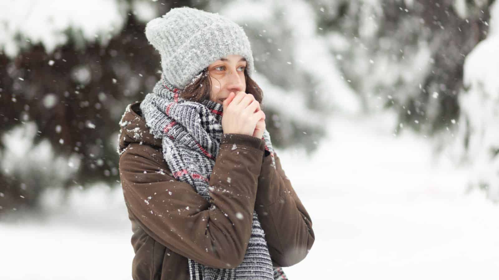 Cold woman in warm clothes in snowy winter weather in park