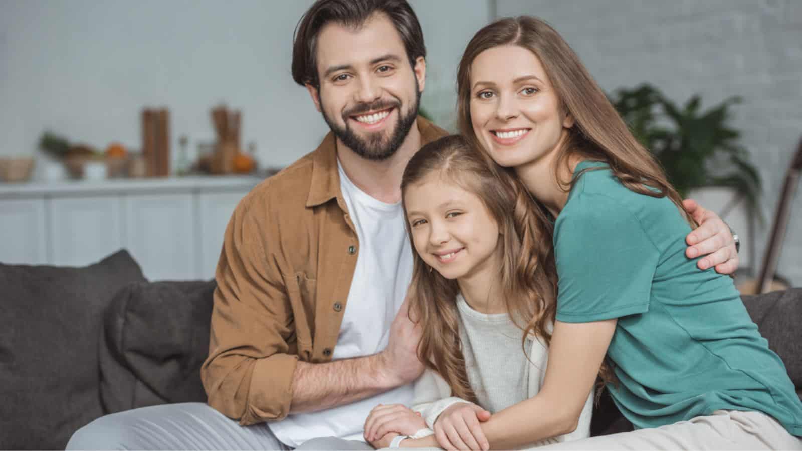Happy parents and daughter looking at camera at home