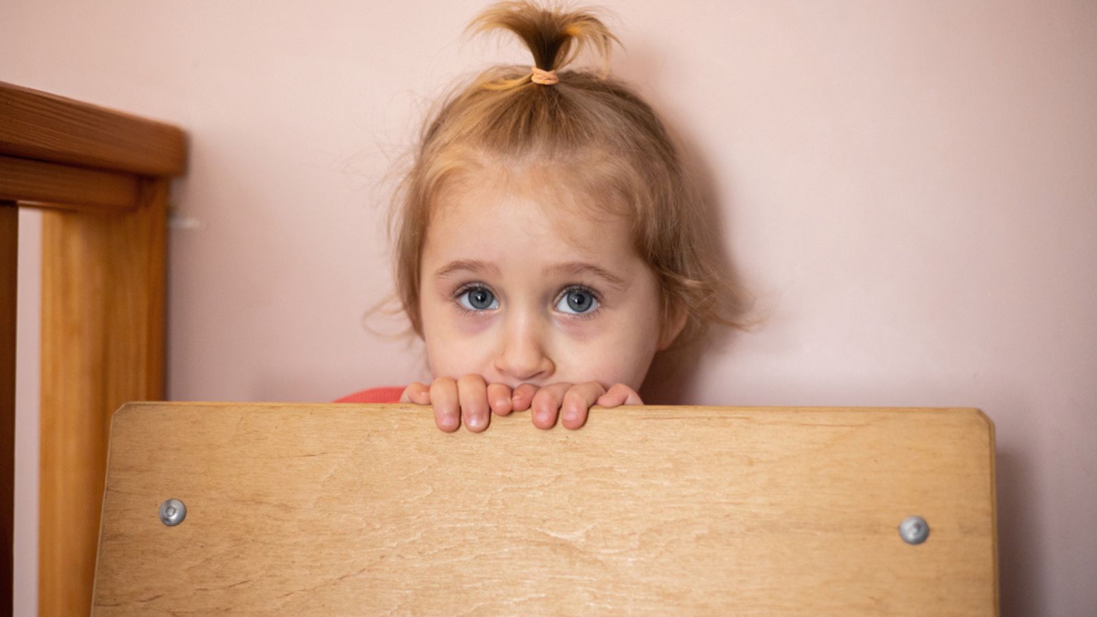 Sad little girl with a toy in her hands hiding