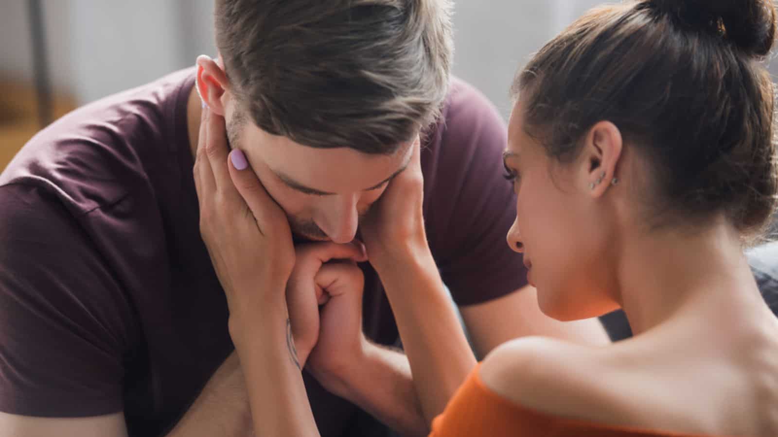 Tender woman calming sad man by touching his face