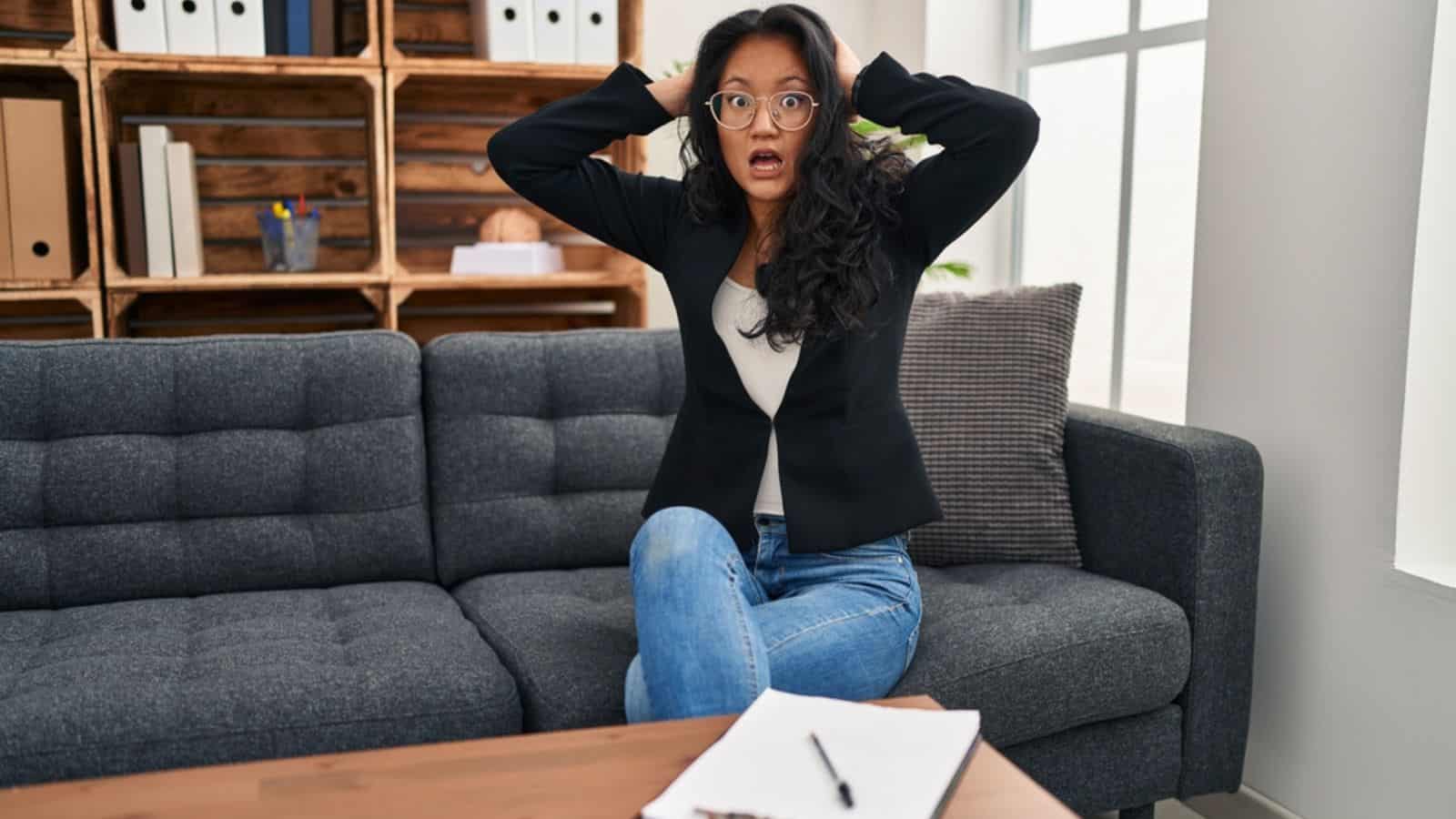 Young Asian woman surprised at consultation office crazy and scared with hands on head