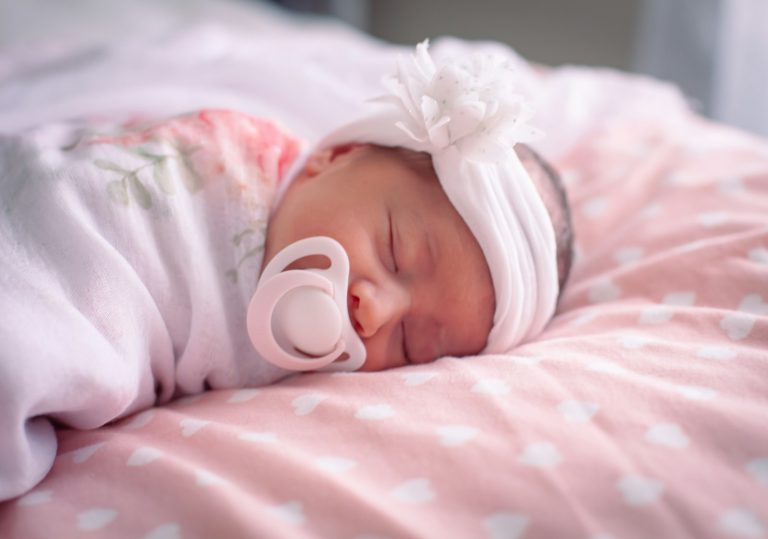 a baby with a pacifier laying on a pink blanket; when to introduce a pacifier