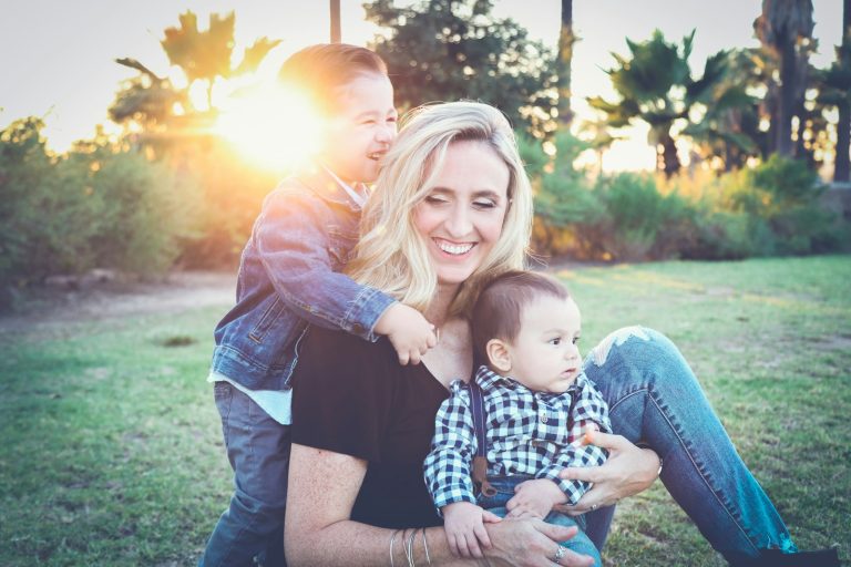 woman holding baby sitting on green grass field under sunset; slow motherhood
