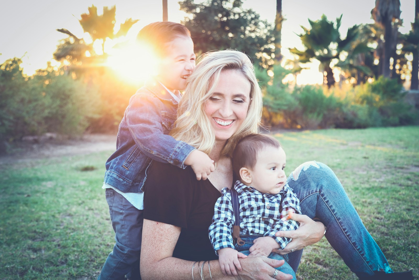 woman holding baby sitting on green grass field under sunset; slow motherhood