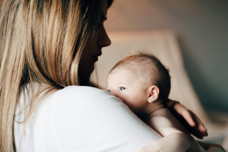 woman in white shirt carrying baby, breast feeding vs. formula feeding