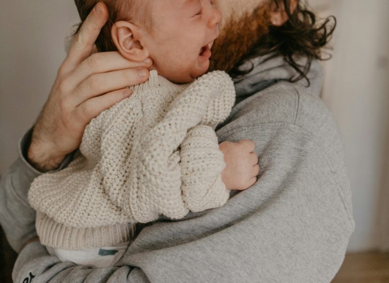 a man holding a baby in his arms; Cry-It-Out vs. No-Cry Sleep
