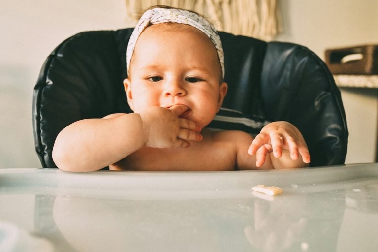 a baby sitting in a high chair eating food; baby-led weaning