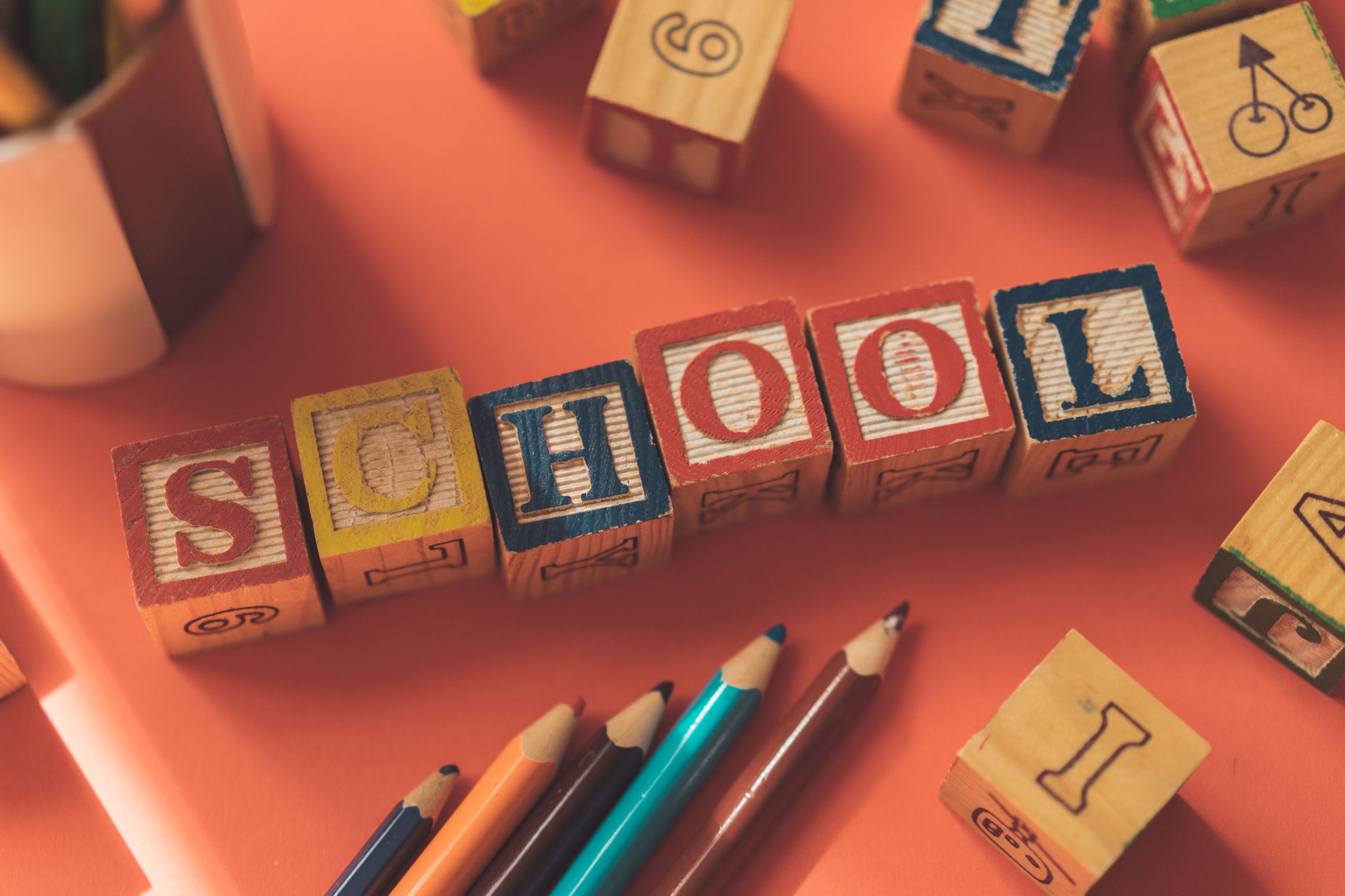 From above of wooden cubes making word school placed near color pencils on red table; back to school 2026