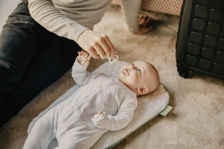 baby in white onesie lying on floor; sleep training