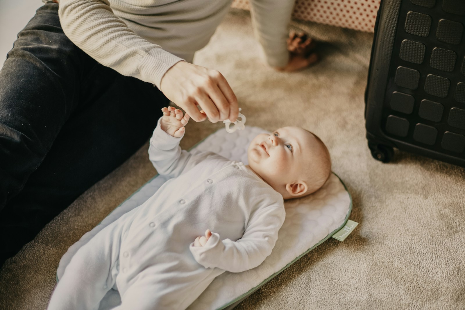 baby in white onesie lying on floor; sleep training