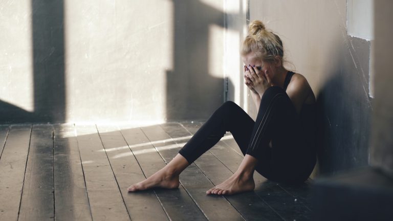 Woman sitting on floor, covering face with hands.; baby blues vs postpartum depression