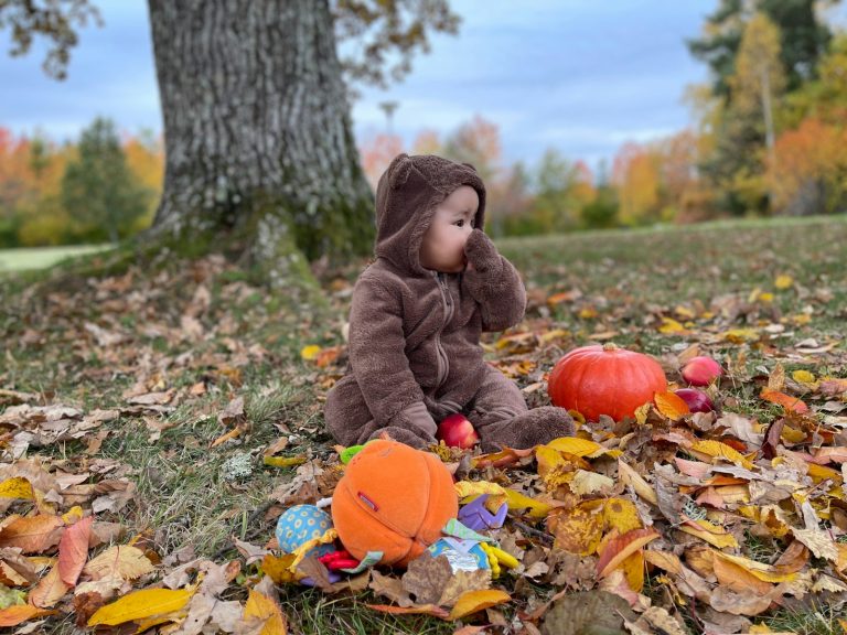 A small child sitting on the ground in a pile of leaves- sensory-friendly