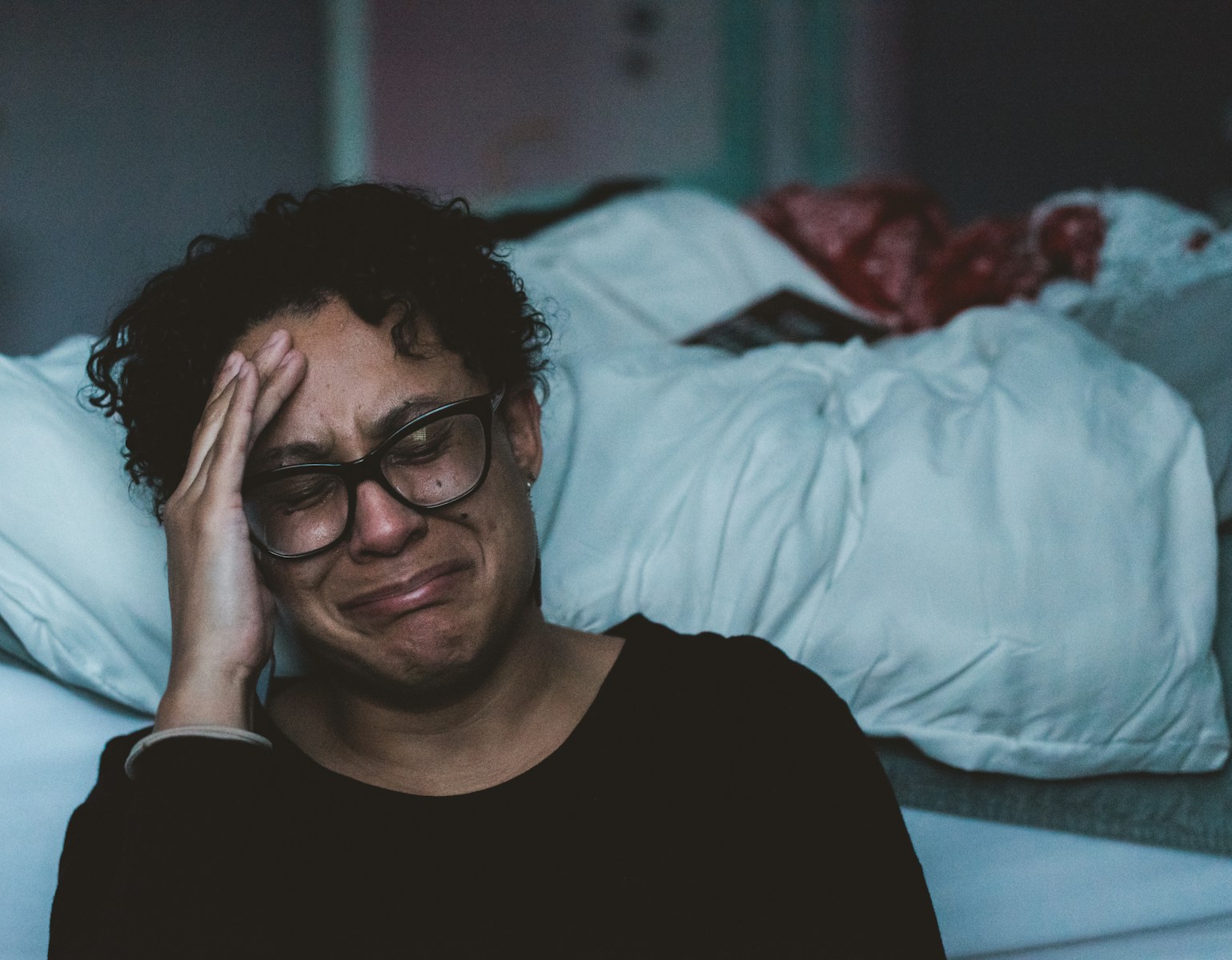 person crying beside bed; Postpartum Depression Vs. Postpartum Psychosis