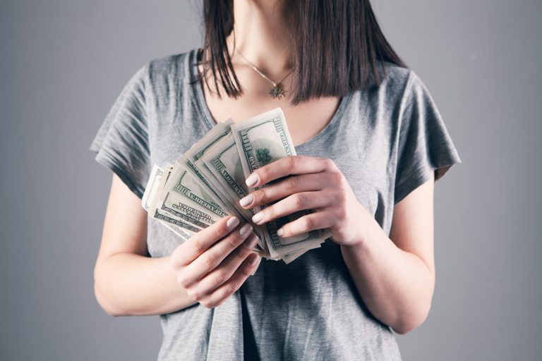 woman in gray shirt holding fan of us dollar bills; cost of raising a child in 2026