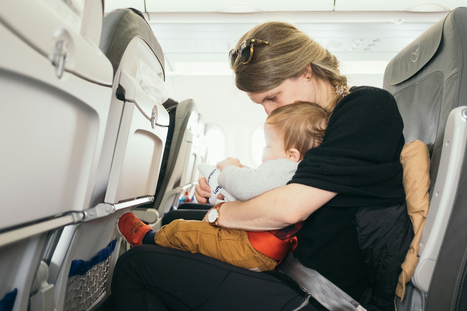 woman carrying baby while sitting on gray seat; travel with a toddler