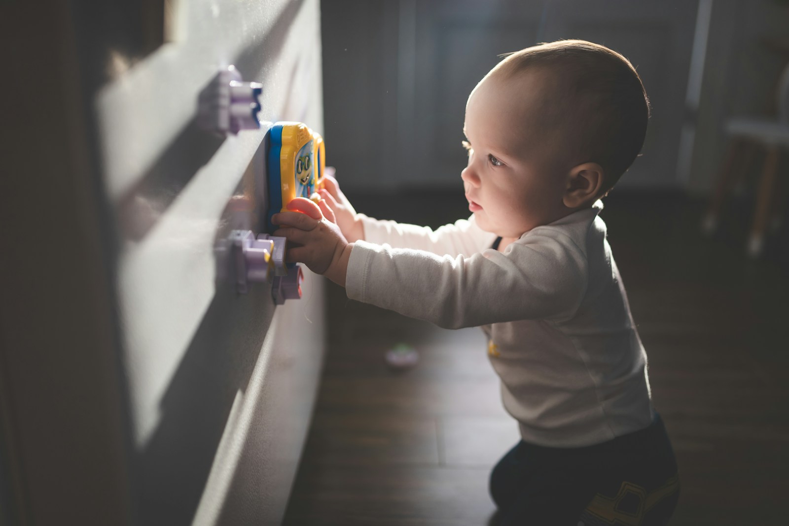 baby in white long sleeve shirt and black pants holding blue plastic toy; childproof