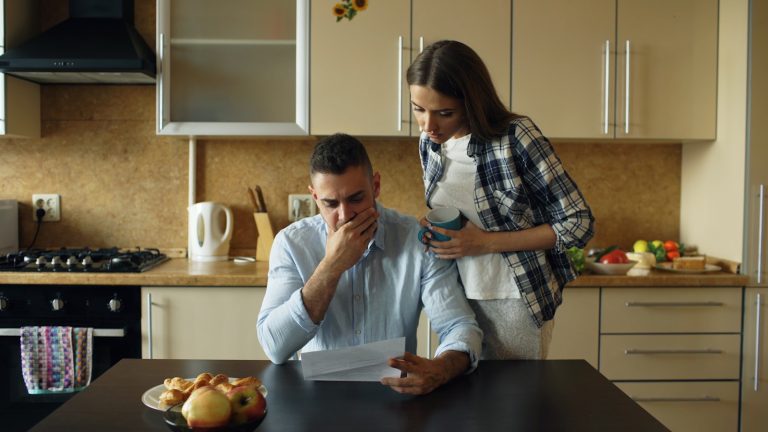 Couple looking stressed over bills at kitchen table.; family budget
