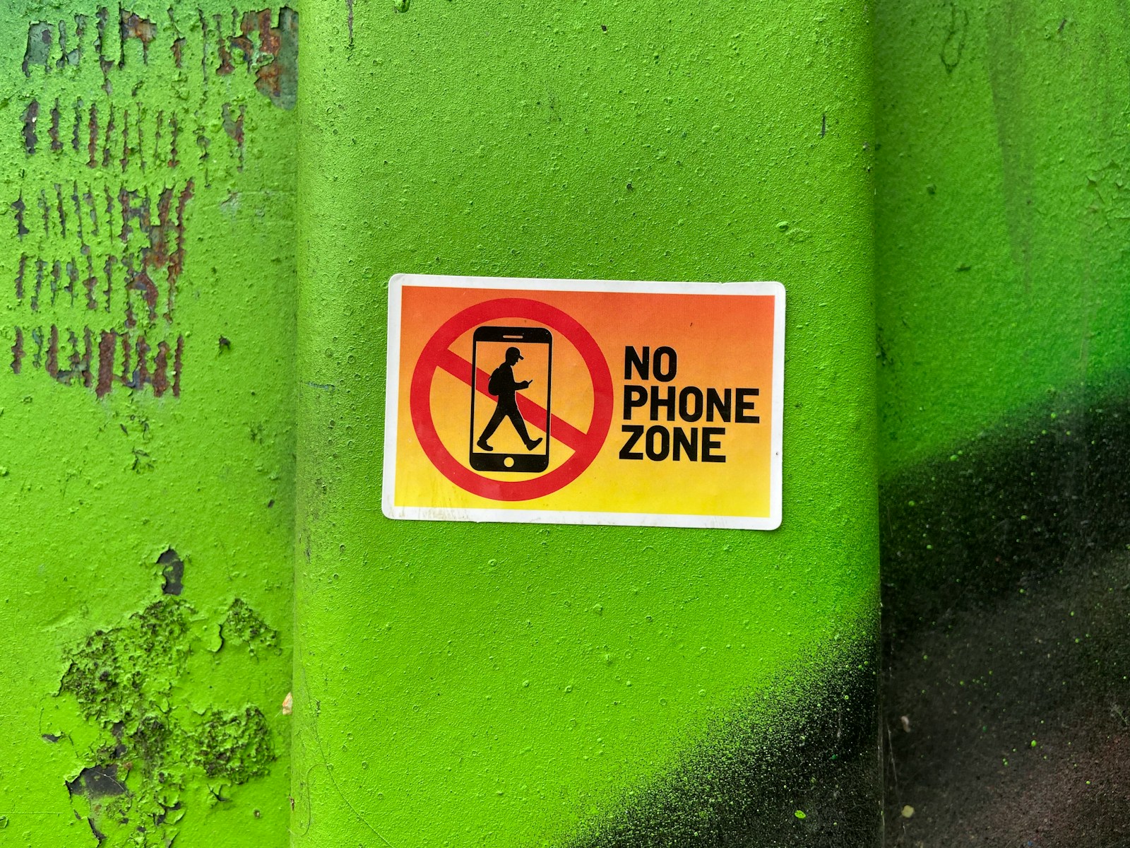 A no phone zone sign on a green wall; phone free childhood