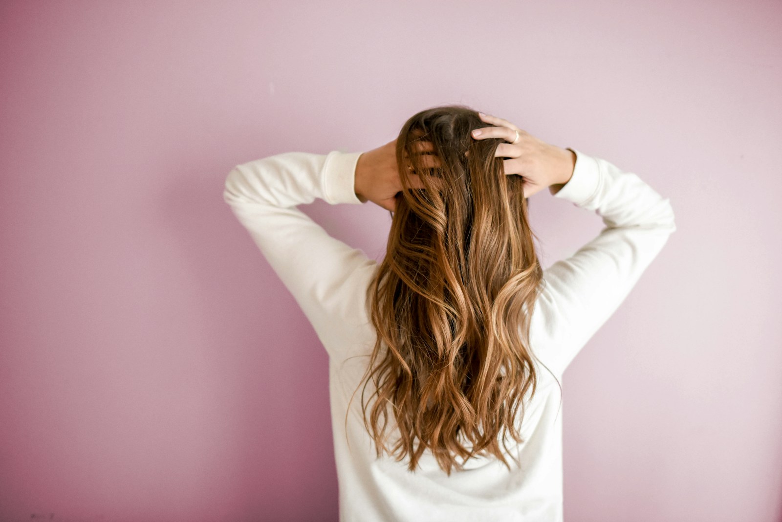 woman in white long-sleeved shirt standing in front of pink wall; postpartum hair loss